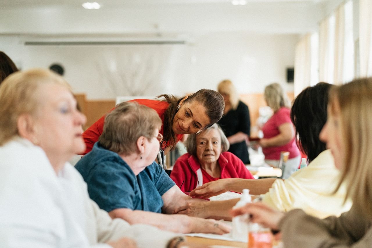 services-04 Smiling caregivers and seniors engage over a table at a community center.