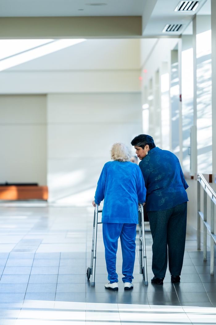 services-03 A nurse assists an elderly woman with a walker in a bright hospital corridor.